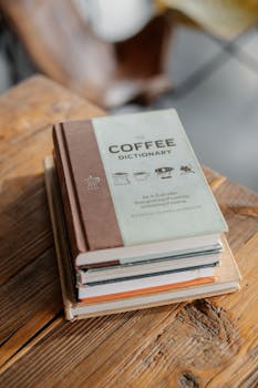 pexels-photo-29036600-29036600 A stack of books on a wooden table with a coffee dictionary on top. Perfect for literary and coffee lovers.