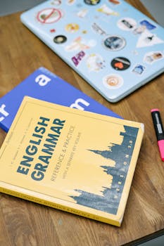 pexels-photo-5676740-5676740 High-angle view of an English grammar book and a laptop with stickers on a wooden desk.